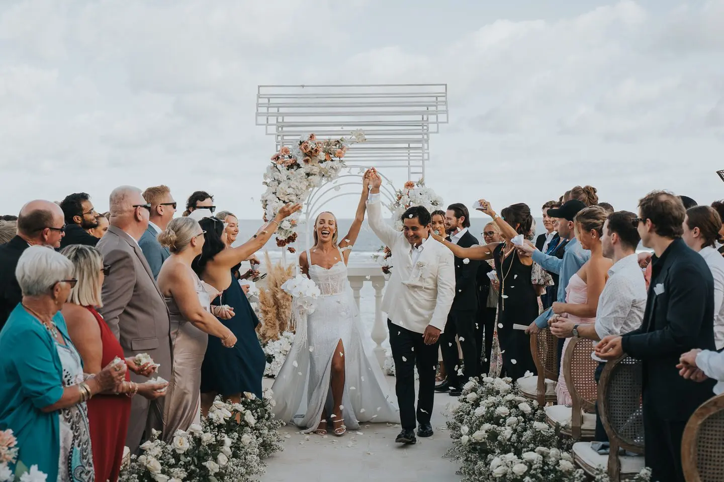 Beachfront wedding ceremony with ocean view at Canna Bali a man and woman holding flowers and standing under a white arch